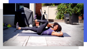 Displays fitness content creator Nadia Santiago performing a bicycle oblique crunch on a fitness mat outdoors